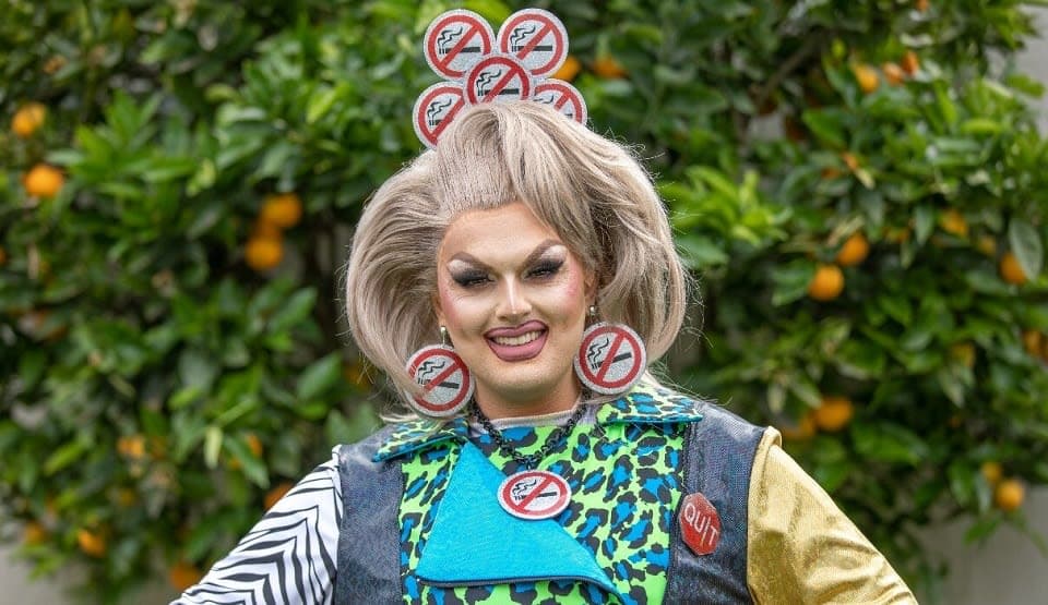 A drag queen in a a crown of quit smoking symbols smiles at the camera