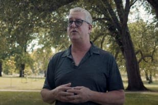 Rick is standing outside in a park speaking to the camera
