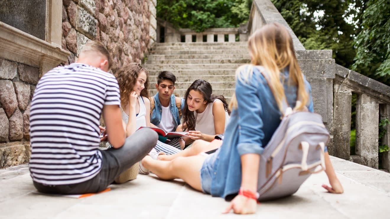 A group of five students sitting and looking at a book