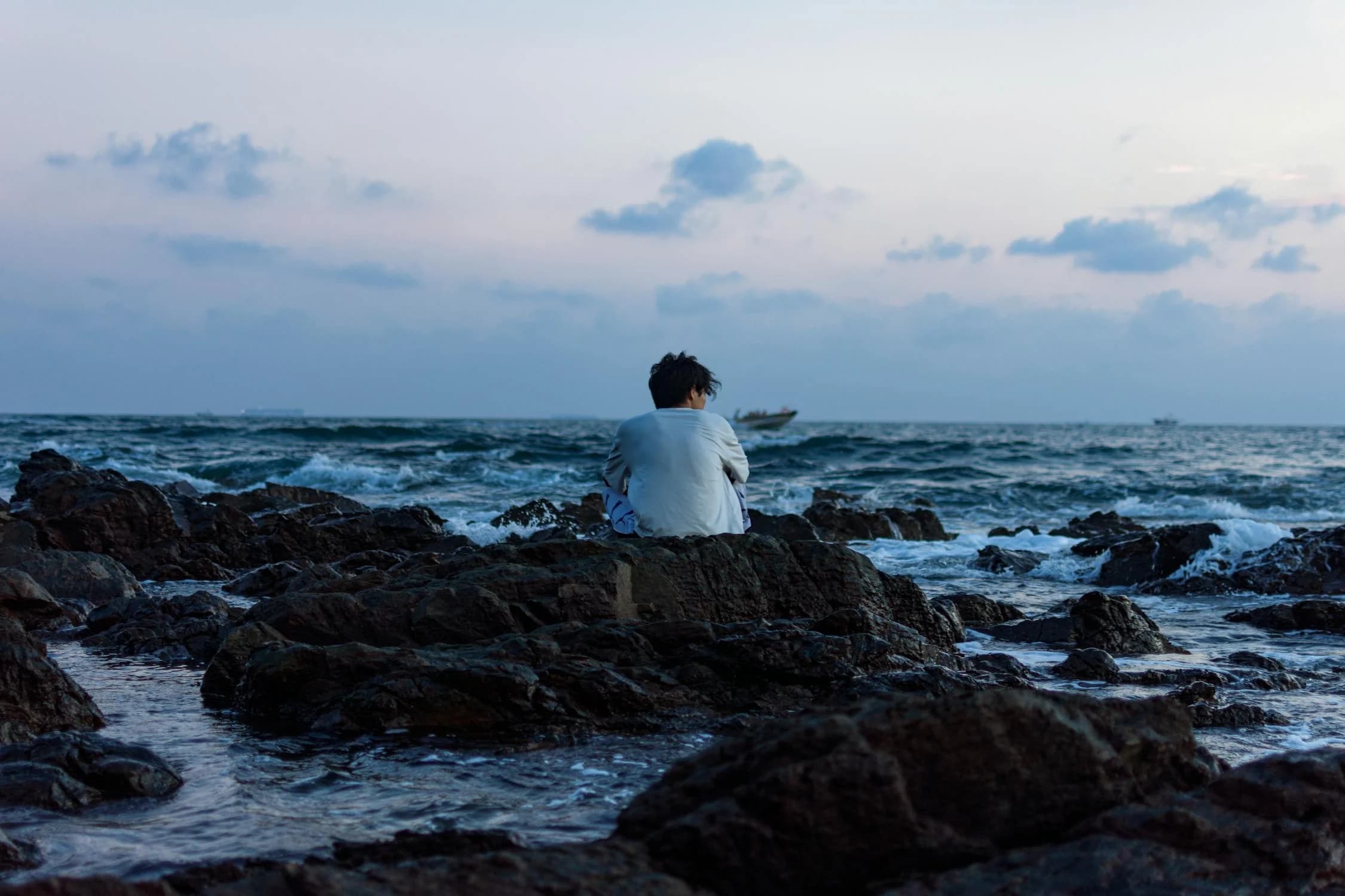 A man sitting on a rock looking out at the ocean
