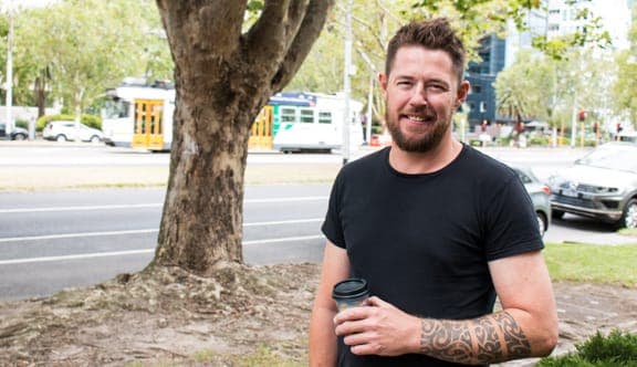 A man smiles at the camera while holding a coffee cup