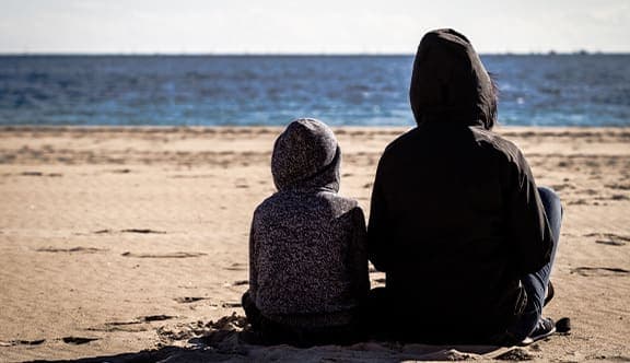 A parent and child sit on the beach