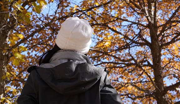 A women wearing a beanie standing outside looking at trees
