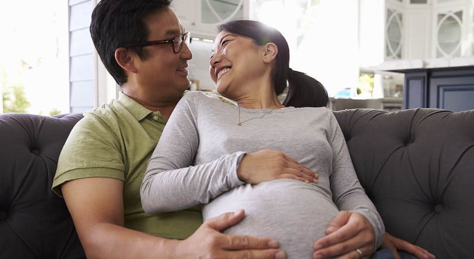 A pregnant woman sitting on a couch smiling at a man