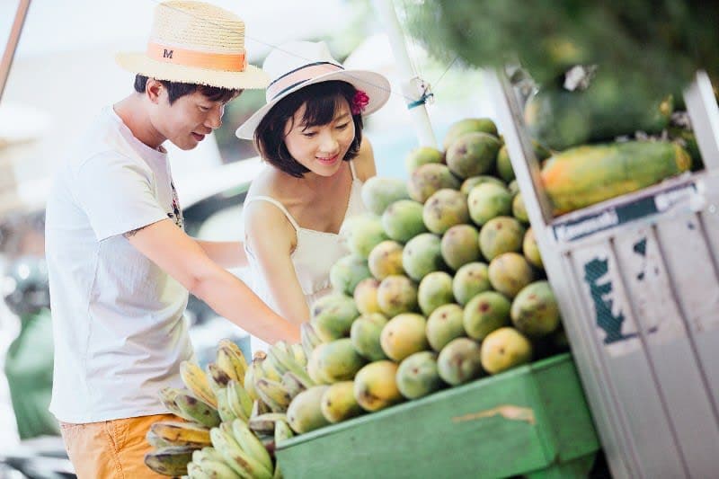 A Chinese woman standing with a Chinese man looking at a stall selling fruit