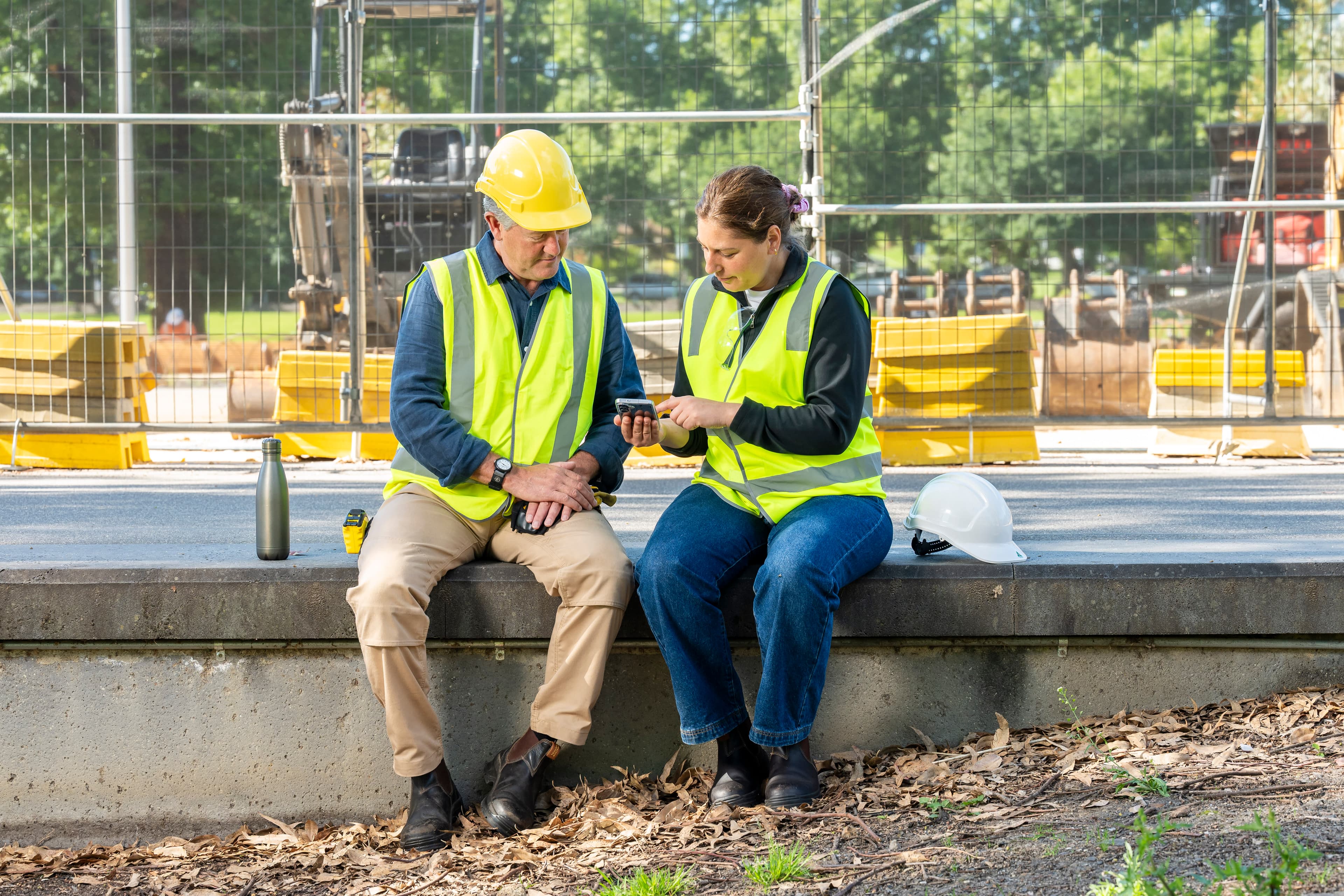 Two people in high-vis clothing consult a phone