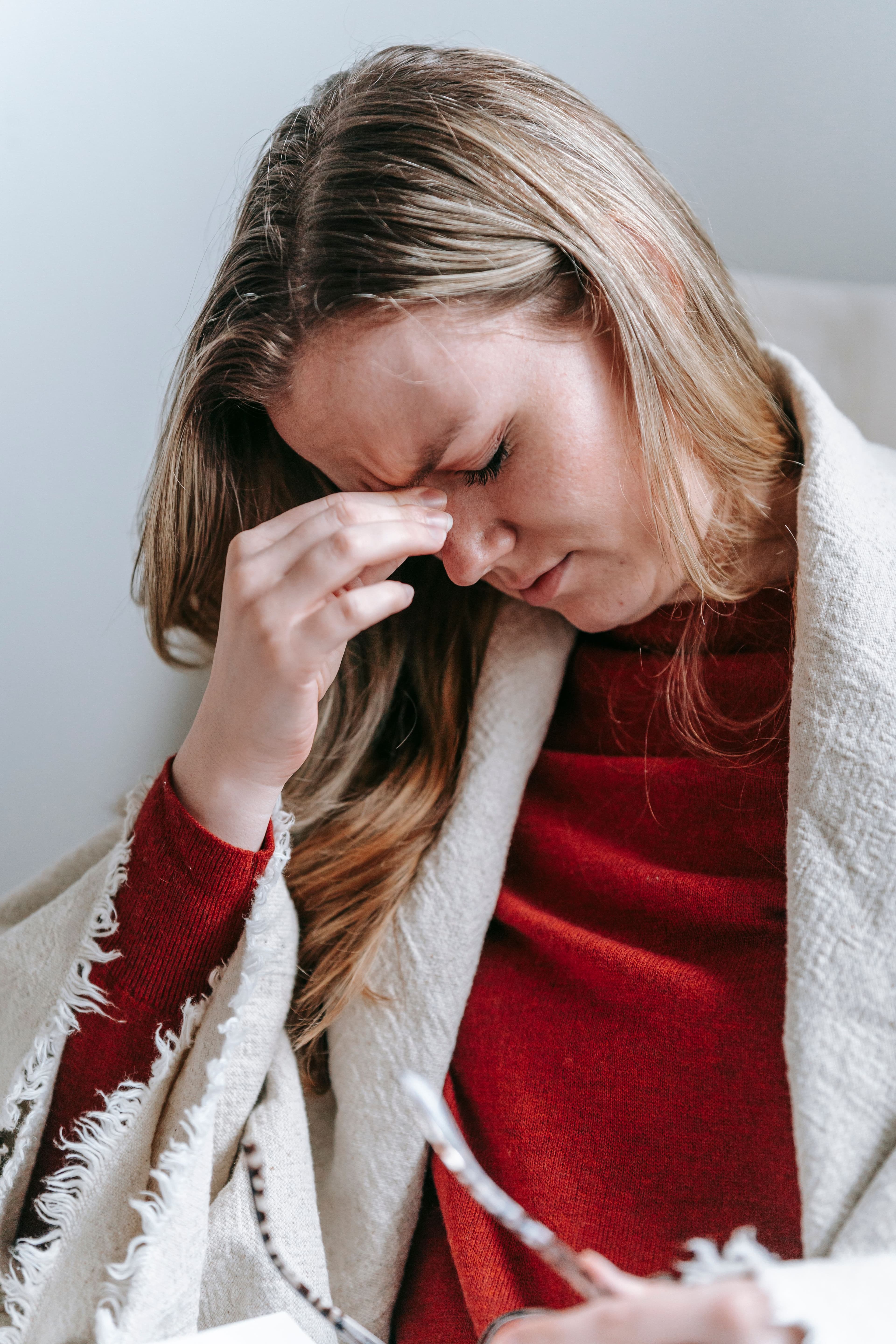 A woman pinches her head as if experiencing a headache. She has a blanket around her shoulders.