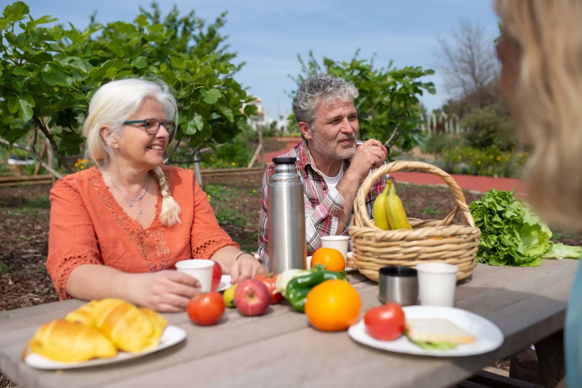 A man and woman sit at a picnic table with fresh fruit and vegetables in front of them.