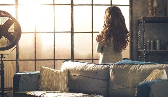 A woman stands in her living room with her back to us, as she looks out the window