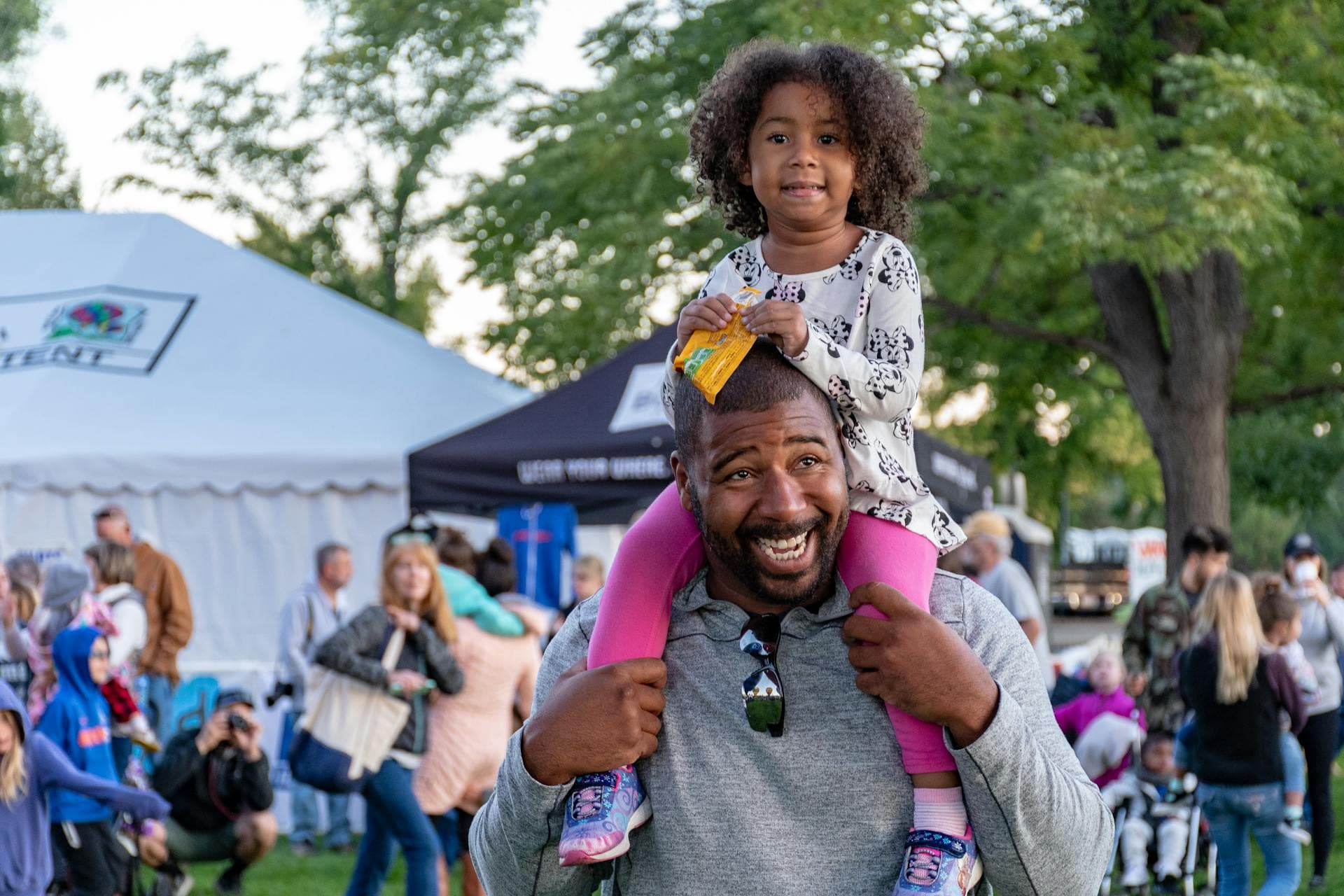 A father walking through a market with his daughter on his shoulders