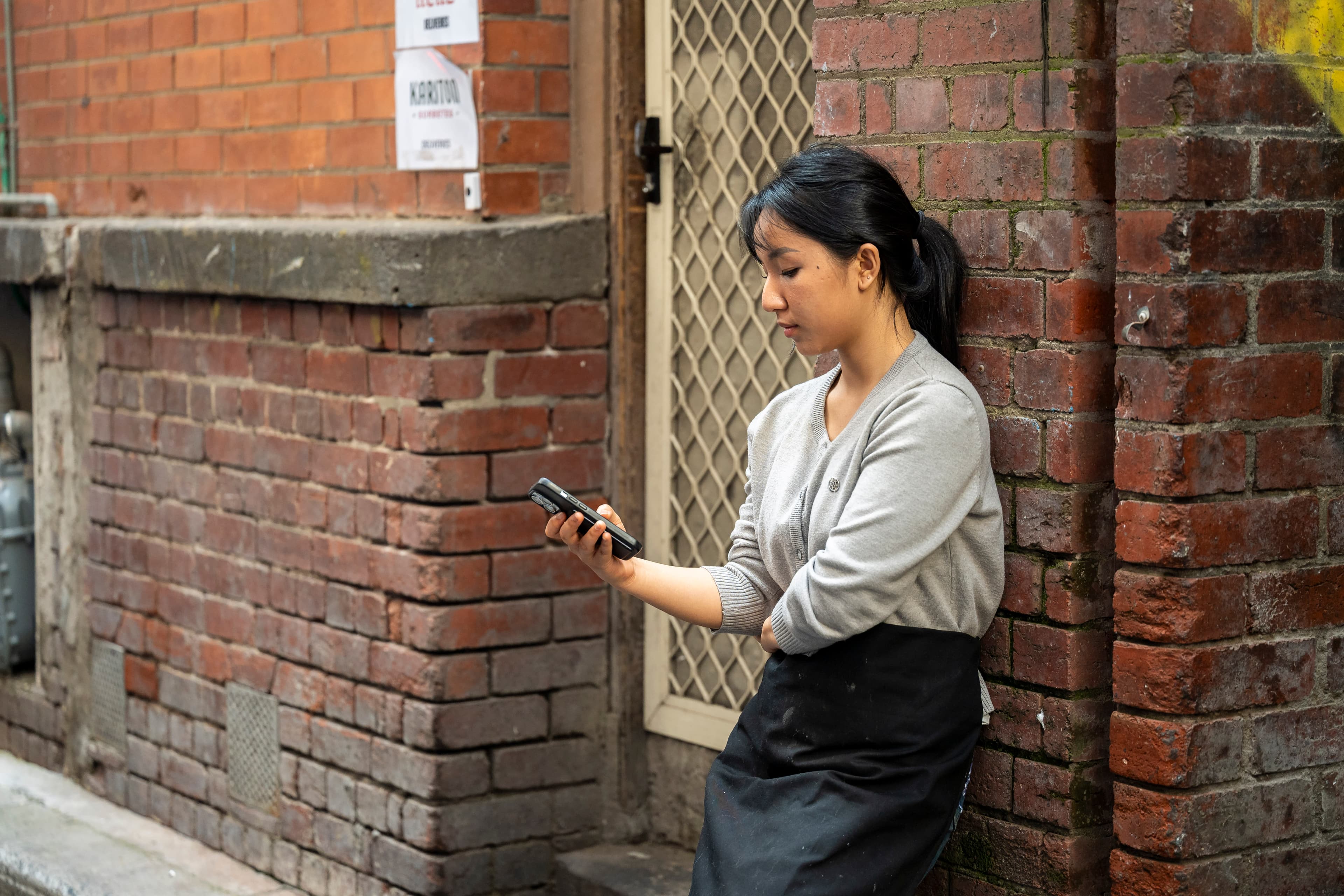 A young woman checks her phone in an alleyway.
